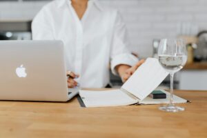 Businesswoman planning her schedule on a desk with a laptop, notebook, and water glass.